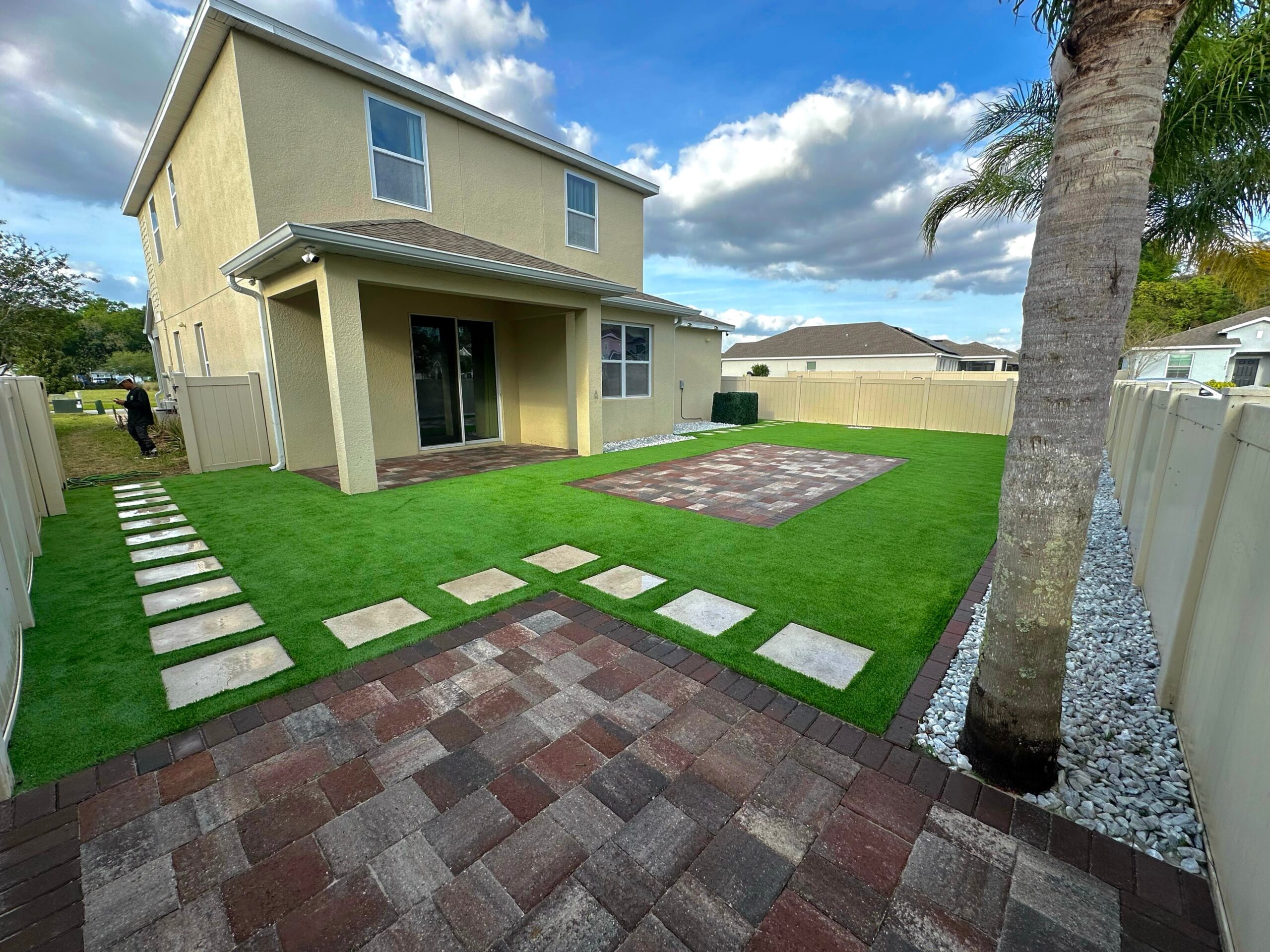 Artificial turf drainage in practice: backyard lawn with paver stepping stones and a patio